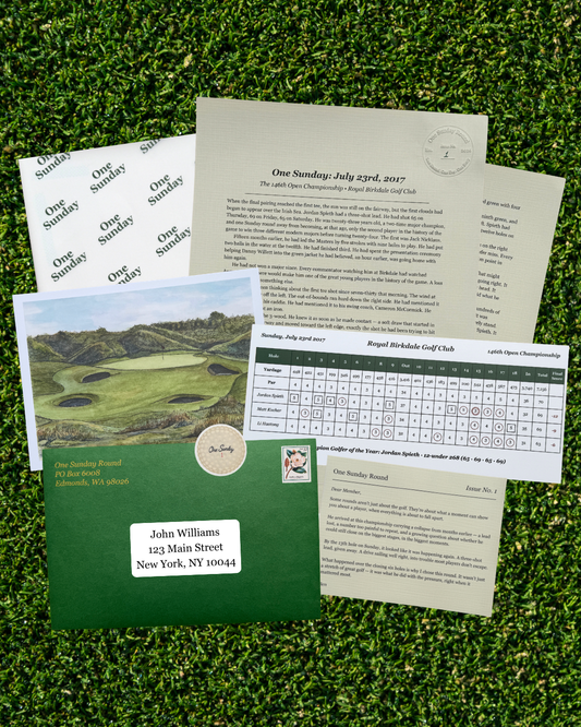 A golf-themed stationery set arranged on artificial grass, including a green envelope with a printed golf course photo, cream letterhead papers, a round-robin sheet, and a name label sticker.
