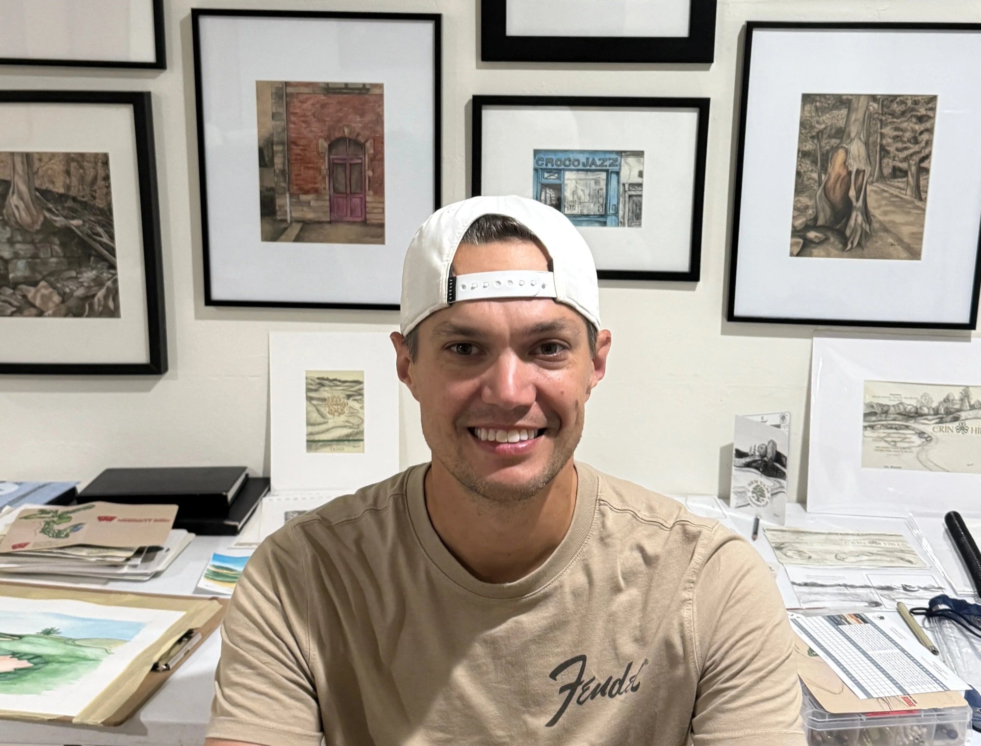 commission artist Joe Woldt sitting at a desk with framed artworks on the wall behind him